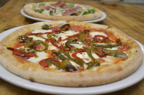 A close-up of a pizza topped with green and red peppers, with another pizza in the background on a wooden table.