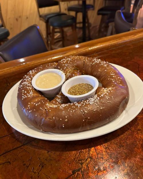 A large pretzel on a plate, served with two dipping sauces in small bowls.