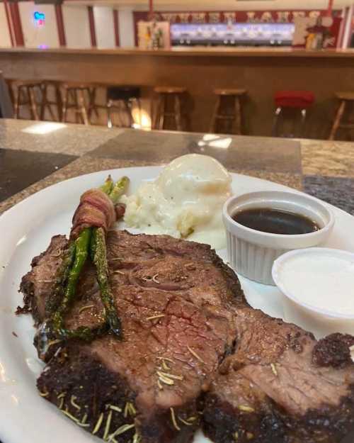 A plate featuring a juicy steak, bacon-wrapped asparagus, mashed potatoes, and dipping sauces.