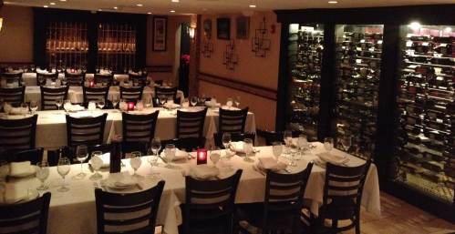Elegant restaurant interior with neatly set tables, wine racks, and soft lighting creating a cozy atmosphere.