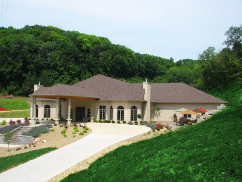 A large, modern house with a landscaped yard, surrounded by trees and a gravel driveway.