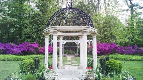 A beautiful garden featuring a stone gazebo surrounded by vibrant purple flowers and lush greenery.