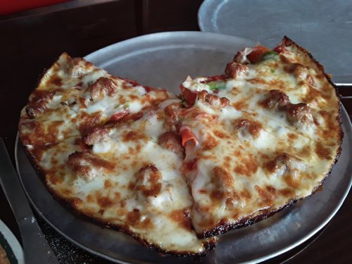 A heart-shaped pizza topped with cheese, pepperoni, and sausage, served on a metal plate.