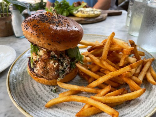A poppy seed bun burger filled with greens and crispy ingredients, served with a side of golden French fries.