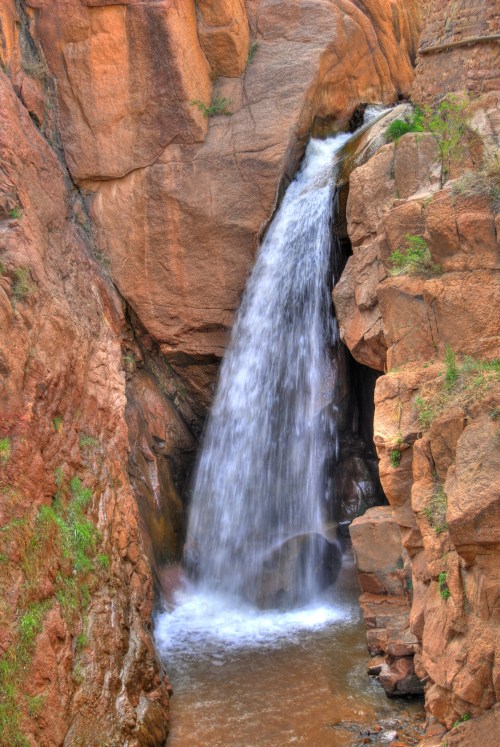 A waterfall cascading down rocky cliffs, surrounded by rugged terrain and greenery.