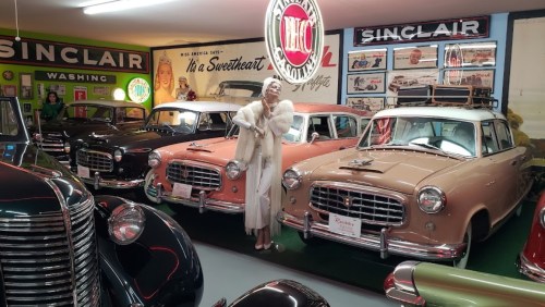 A vintage car museum display featuring classic cars and a woman in 1920s attire, surrounded by retro signage.