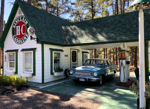 A vintage Sinclair Gasoline station with a classic blue car parked outside, surrounded by trees.