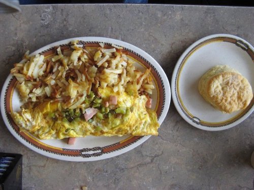 A plate with a vegetable and ham omelet, hash browns, and a biscuit on the side.
