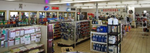 A wide view of a convenience store interior filled with shelves of products, including snacks, drinks, and automotive supplies.