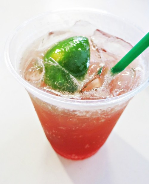 A refreshing drink in a clear cup with ice, a slice of lime, and a green straw.