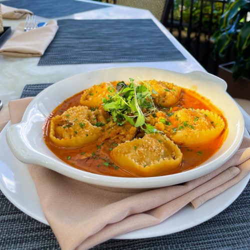 A plate of stuffed pasta shells in a rich tomato sauce, garnished with herbs and breadcrumbs, served on a table.
