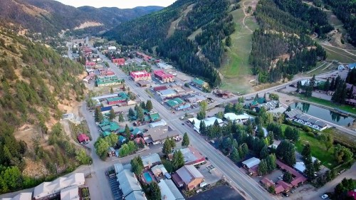 Aerial view of a small mountain town with colorful buildings, trees, and a ski slope in the background.