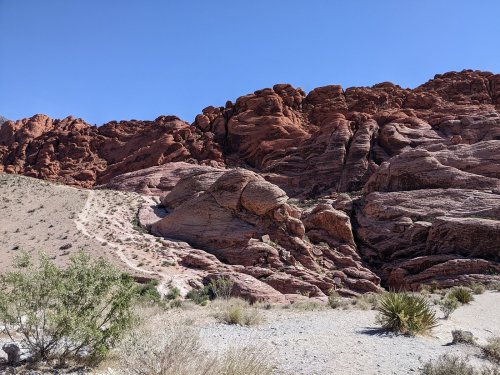 A rugged landscape featuring red rock formations and sparse vegetation under a clear blue sky.