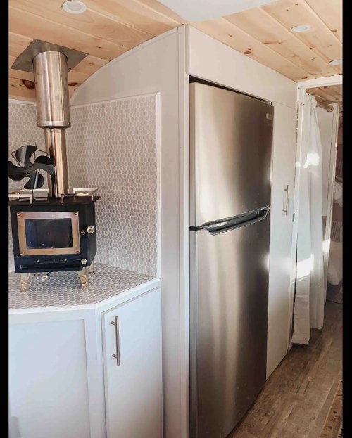 A cozy kitchen area featuring a stainless steel fridge, a small stove, and wooden ceiling details.
