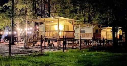 Cozy glamping tents illuminated at night, surrounded by trees and soft lighting in a serene outdoor setting.