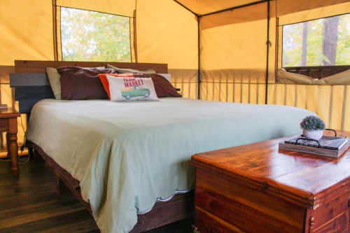 Cozy tent interior featuring a queen bed with a light green cover, wooden furniture, and large windows.