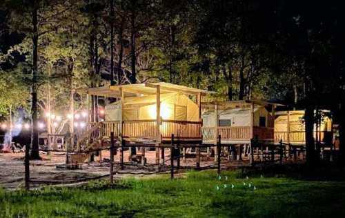 Cozy cabins illuminated at night, surrounded by trees and string lights, creating a warm, inviting atmosphere.