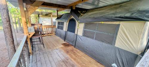 A wooden deck with a large tent structure, surrounded by trees in a natural setting.