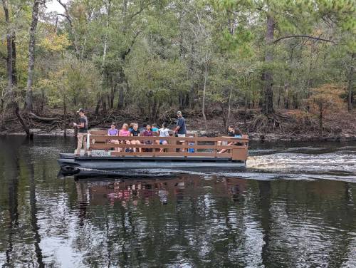 A group of people on a boat in a calm river, surrounded by trees and nature.