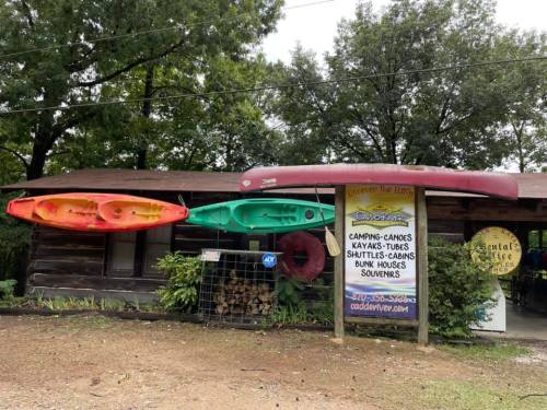 A rustic cabin with colorful kayaks and canoes displayed outside, advertising outdoor activities and souvenirs.