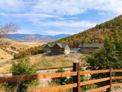 A scenic view of a house on a hillside, surrounded by colorful autumn foliage and mountains in the background.