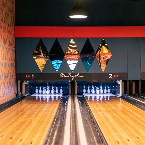 Two bowling lanes with polished wooden floors and colorful diamond-shaped mirrors in the background.
