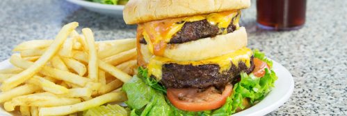 A towering cheeseburger with two patties, melted cheese, lettuce, and tomato, served with a side of golden fries.