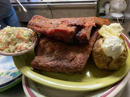 A plate featuring smoked ribs, coleslaw, and a baked potato topped with sour cream.