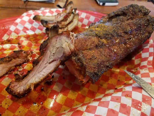 A plate with a large piece of smoked meat and several rib bones, all on a red and white checkered paper.