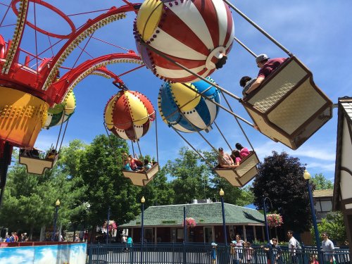 Colorful hot air balloon rides at an amusement park, with people enjoying the view against a clear blue sky.