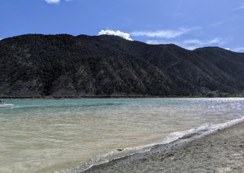 A serene landscape featuring a calm lake with turquoise water, surrounded by mountains under a clear blue sky.