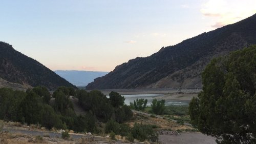 A serene landscape featuring mountains, a river, and trees under a soft sunset sky.