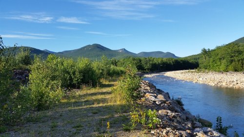 A serene river winding through lush greenery, with mountains in the background under a clear blue sky.