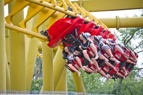 A group of thrill-seekers enjoying a roller coaster ride, suspended upside down against a bright yellow structure.