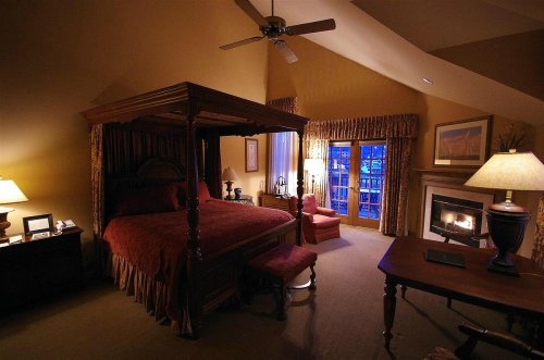 Cozy bedroom with a four-poster bed, warm lighting, and a view of a window with blue curtains.