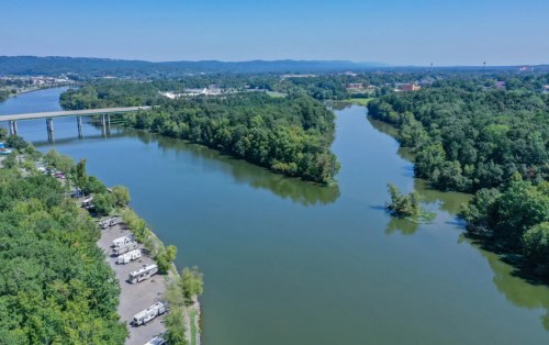 Aerial view of a river winding through lush greenery, with a bridge and RV park visible along the banks.