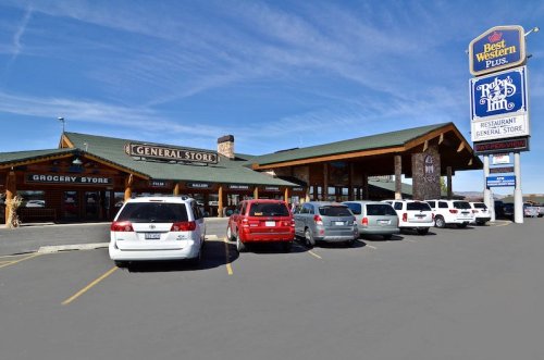A general store with a restaurant sign, featuring parked cars in front and a clear blue sky above.