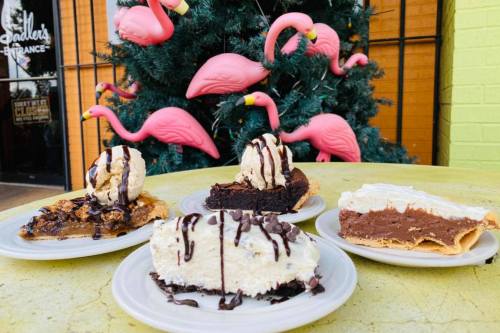 Four dessert plates featuring pies topped with ice cream and chocolate drizzle, set against a backdrop of pink flamingos.