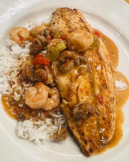 A plate of seasoned fish fillet topped with shrimp and vegetables, served over a bed of white rice.