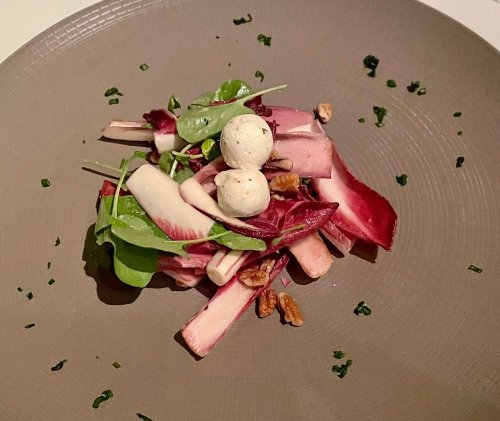 A gourmet salad featuring mixed greens, radicchio, apple slices, pecans, and small cheese balls on a textured plate.