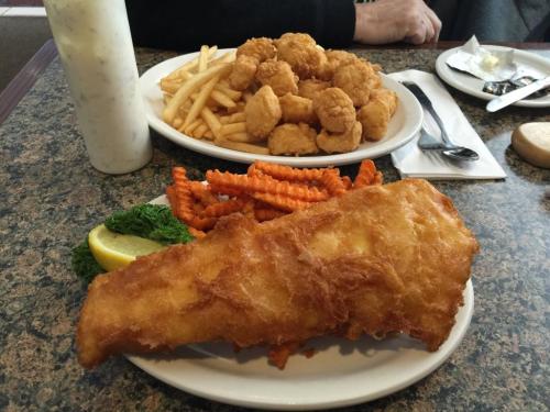A plate of golden fried fish with lemon and greens, accompanied by sweet potato fries and a side of fried shrimp.