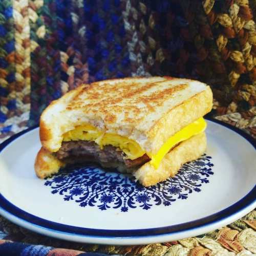 A half-eaten sandwich with a grilled patty and melted cheese on toasted bread, placed on a decorative plate.