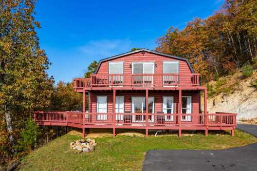 A red two-story house with a large deck, surrounded by autumn trees and a clear blue sky.