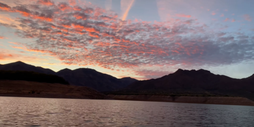 A serene lake at sunset, with vibrant clouds and mountains silhouetted against the colorful sky.