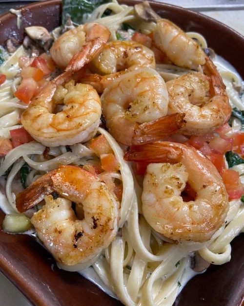 A plate of fettuccine topped with sautéed shrimp, tomatoes, and spinach in a creamy sauce.