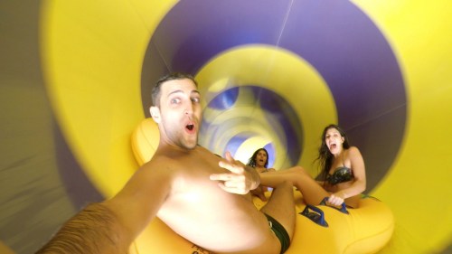 A group of three people enjoying a water slide, smiling and having fun as they descend through a colorful tunnel.