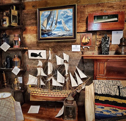 A display of nautical decor featuring a model ship, paintings, and vintage lanterns against a rustic wooden backdrop.