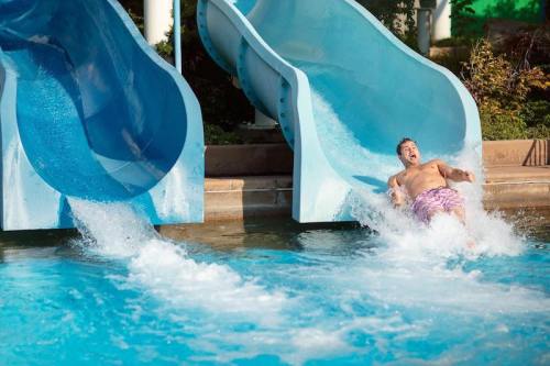 A man splashes into a pool while sliding down a blue water slide on a sunny day.
