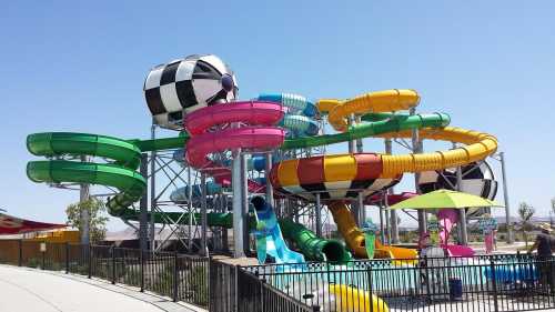 Colorful water slides of various shapes and sizes at a water park under a clear blue sky.