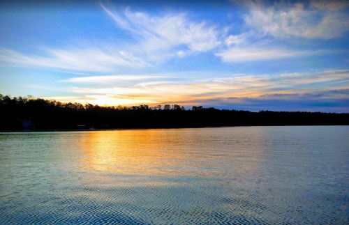 A serene lake at sunset, reflecting vibrant colors in the water with a silhouette of trees along the shore.